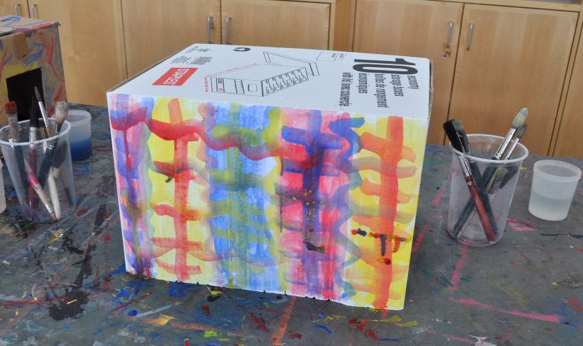 A large copy paper box painted with colorful watercolor lines and patterns.