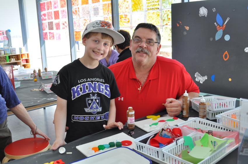 A younger and older guest in the Art Studio smiling while making collaged mixed-media caterpillars.