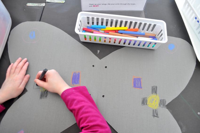 A young guest draws a symmetrical pattern of rectangles onto their wings using crayons.
