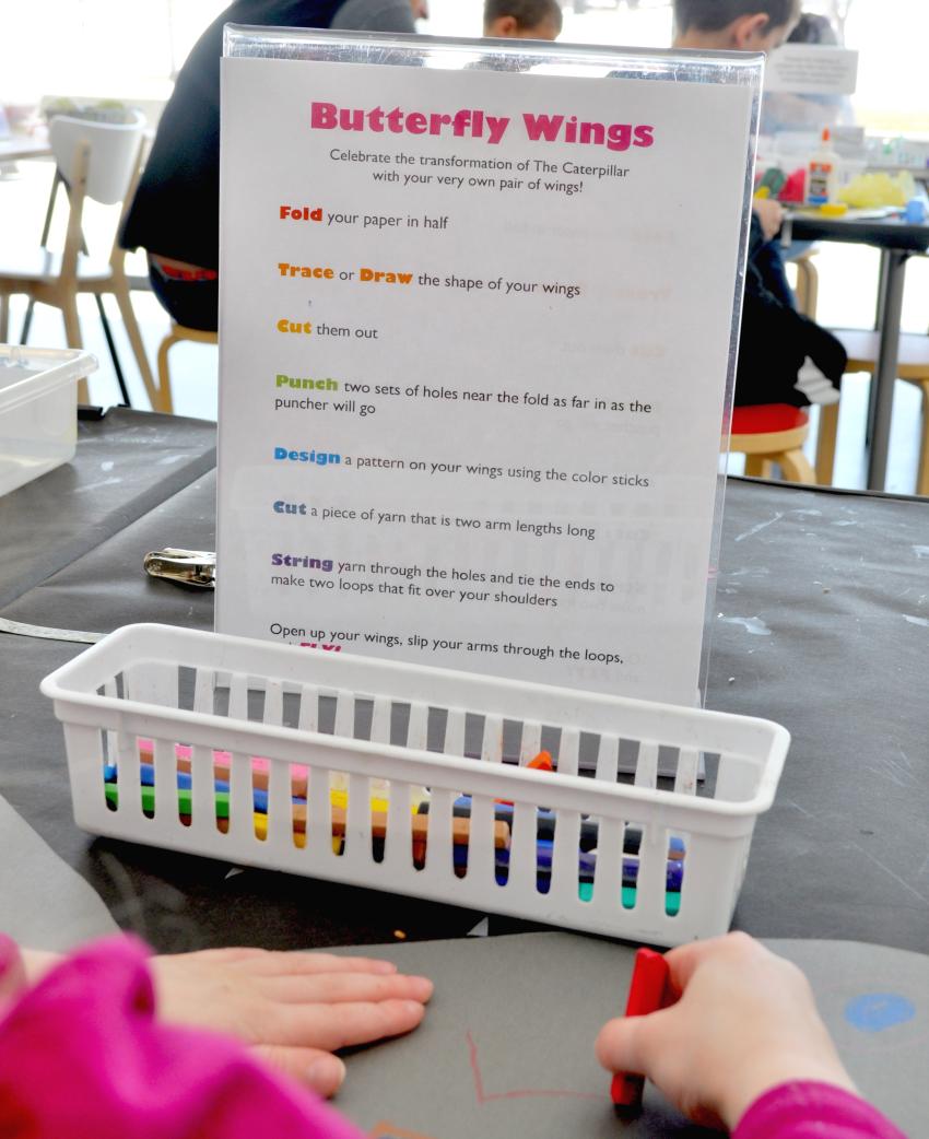 A sign on a table that walks through steps to create wings, including folding papers and drawing patterns on them.