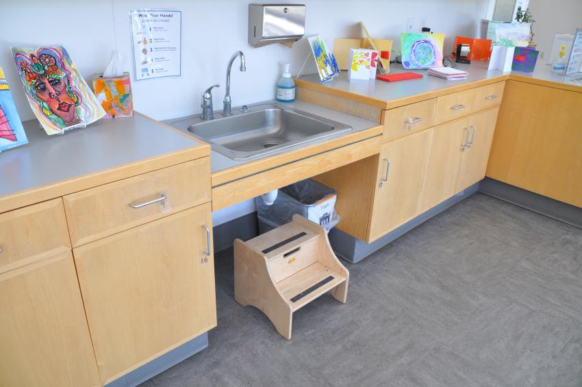 A small wooden step stool underneath a sink in the Art Studio.