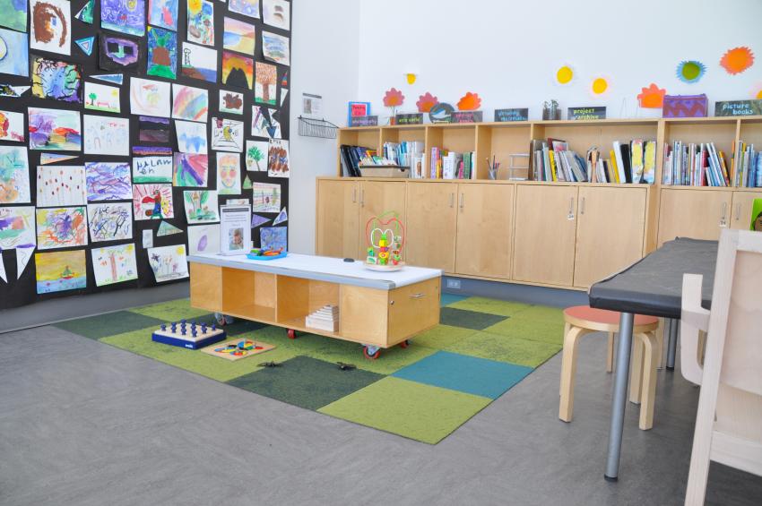 A low drawing table with crayons and toys on top of it and a colorful carpet area beneath it.