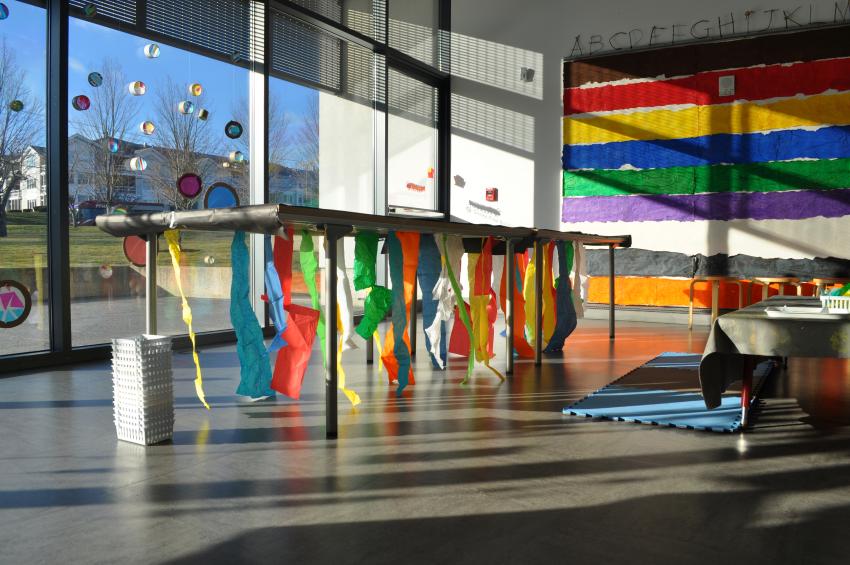 A table with colorful strips of tissue paper taped underneath it, catching the bright light from the large studio windows.