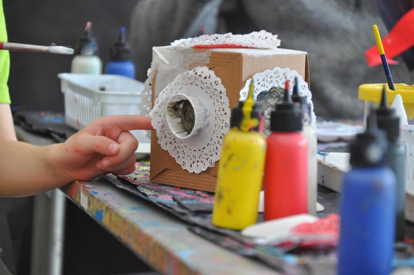 A young artist holds back a doily on their artwork while applying glue.