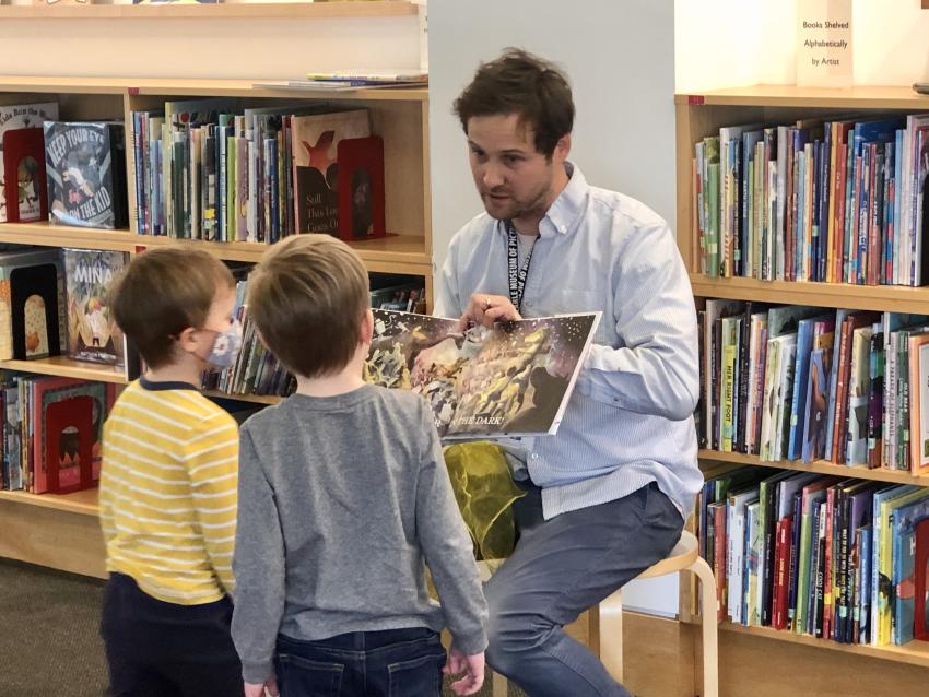 Staff member holding book while two children look closely at the pictures.