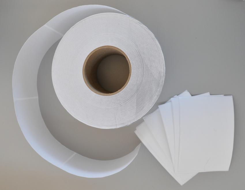 A roll of white labels next to a stack of rectangle labels. 