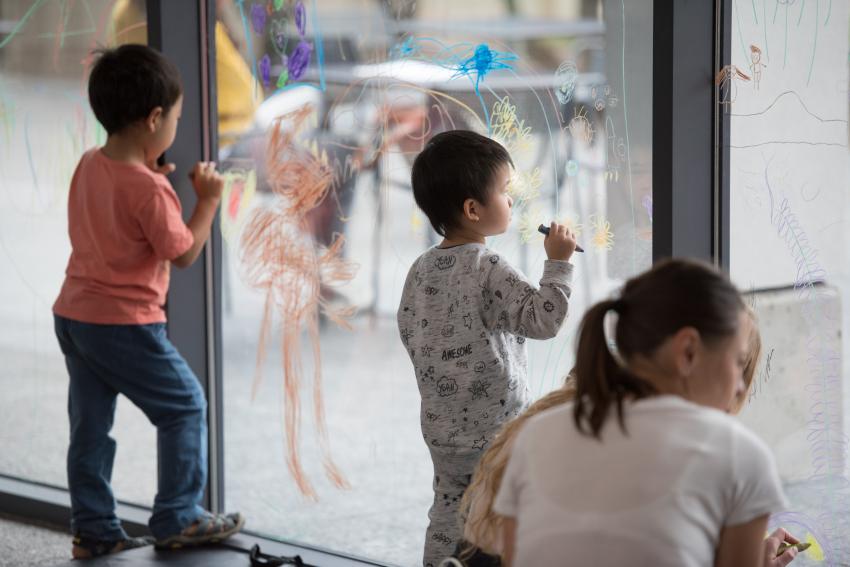 Young guests draw on the window with watercolor pencils, one child takes a break to look at their drawing.