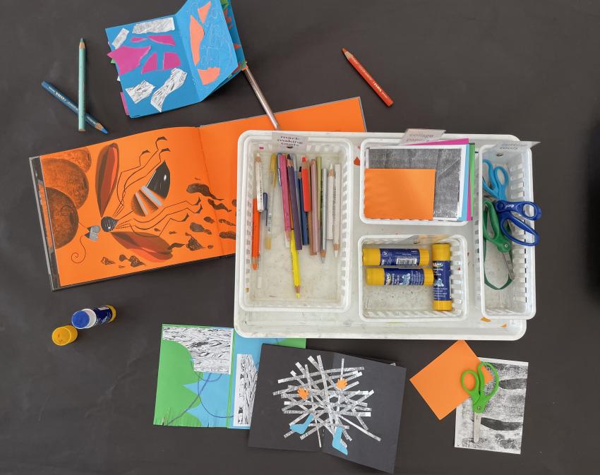 Overhead view of supplies on a table. Books being worked on, scissors, glue, collage papers scattered across work table.