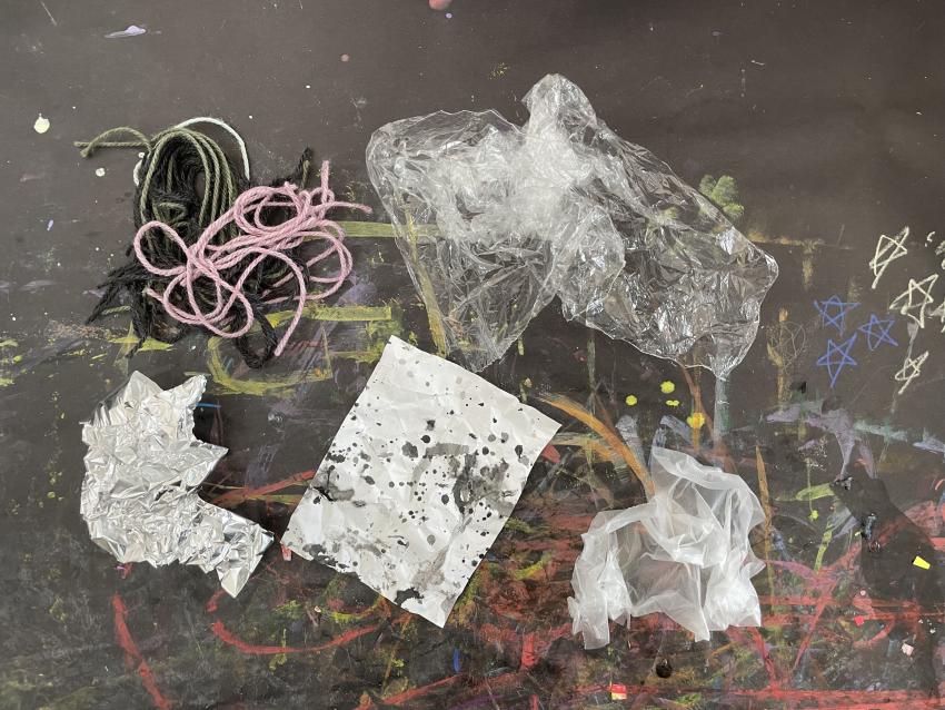 Materials on prep table starting in the upper left corner going clockwise: yarn, scrunched up stretchy plastic, cling wrap, black ink on white paper, tin foil.