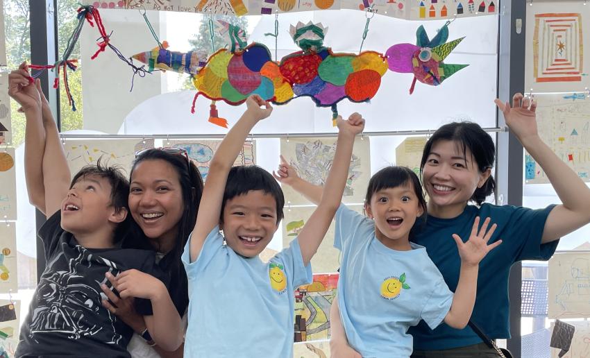 Two adults and three children point above in excitement to their floating paper dragon creation!