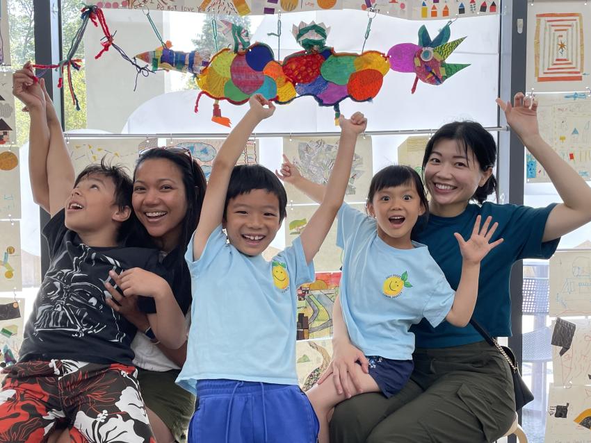 Two adults and three children point above in excitement to their floating paper dragon creation!