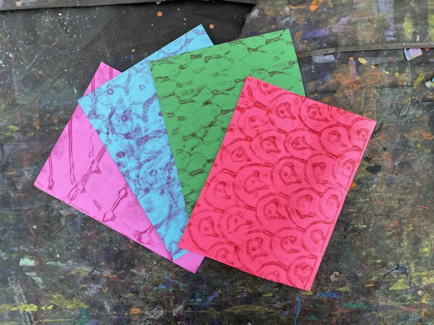 Colorful sheets of collage paper with patterned texture rubbings.