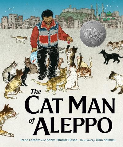 A bearded man wearing a blue and red coat holds out a piece of food to a cat standing on its hind legs reaching for the food. Multiple cats follow the man.