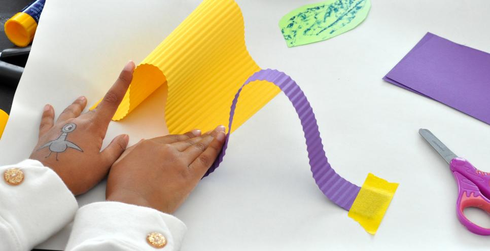Child's hands curving strips of yellow and purple paper.