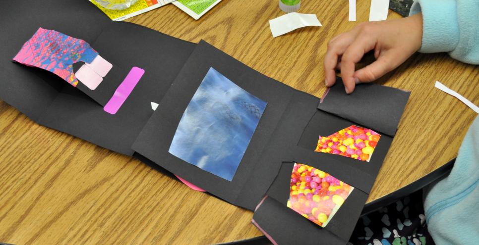 A child pulling back lift flaps on their black accordion fold book to reveal colorful red collage papers.