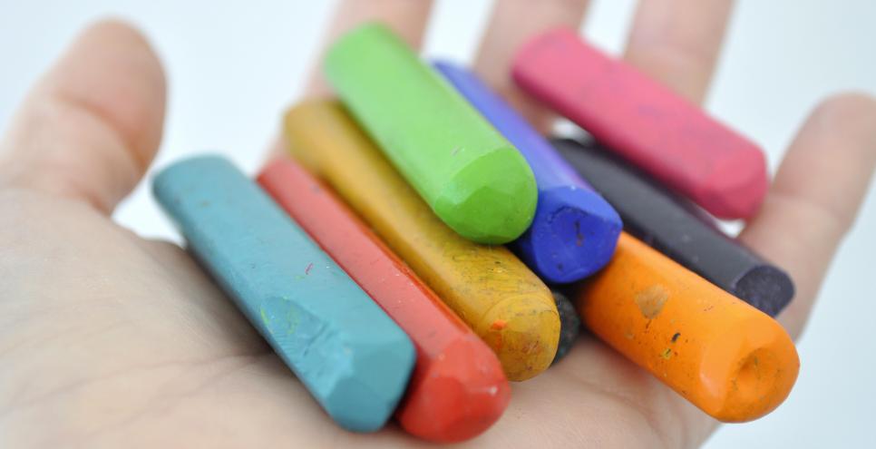 a child's hand holds beeswax crayons in many different colors