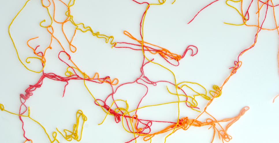 Red, orange, and yellow yarns on a white wall.