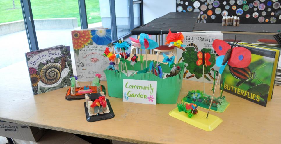 A community garden sculpture made of tissue paper collages with a backdrop of picture books about nature.
