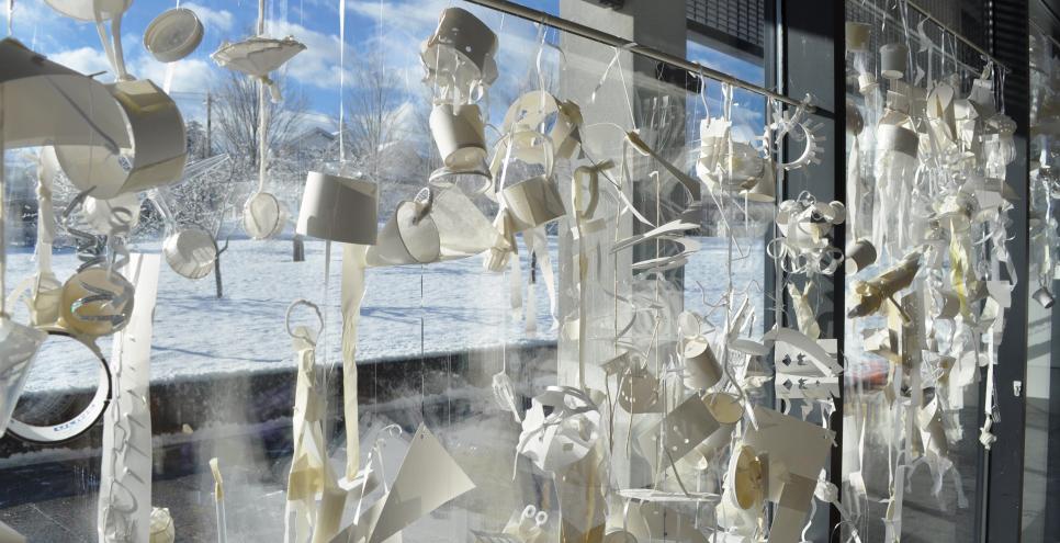 A window filled with white mobiles with a snowy day outside.