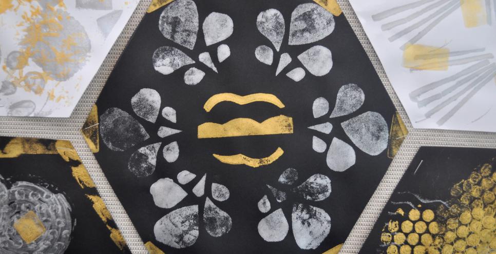 A hexagon-shaped piece of black construction paper with gold and silver stamped shapes on it.