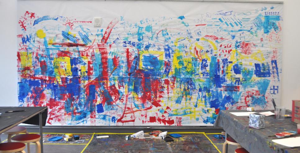 A mural with red, yellow, and blue paint, created by printing with boxes on a white paper backdrop.