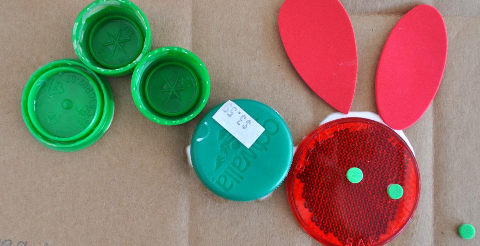 A Very Hungry Caterpillar made from red and green found materials including bottle caps and styrofoam shapes.