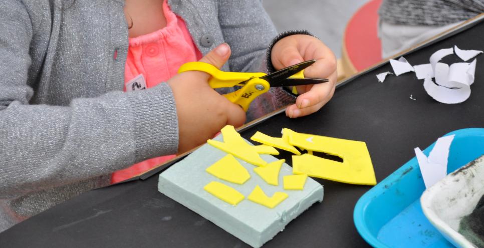 A child cuts yellow self-adhesive foam into shapes to add to her stamp base.