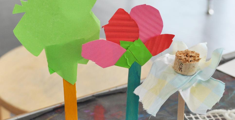 Three flower sculptures made from found materials including papers, corks, ribbons, and popsicle sticks.