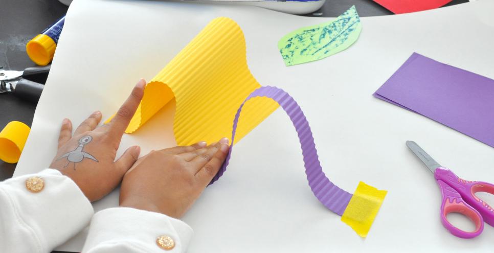 A young child bends yellow paper to attach to their white background paper.