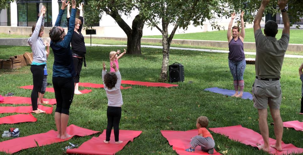 Children and adults doing yoga poses on red mats in the museum's meadow.