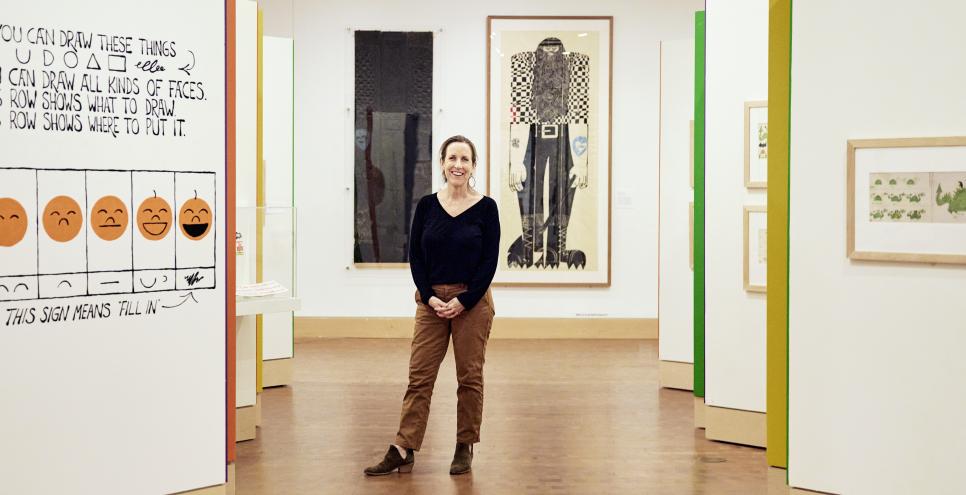 Alix Kennedy standing in gallery at The Carle with Ed Emberley artwork in background