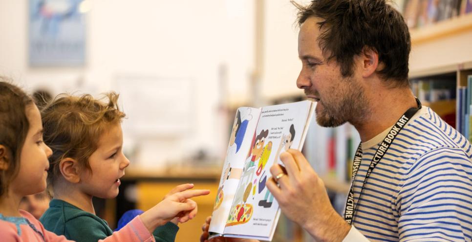 adult holding a book while two kids point at the pages