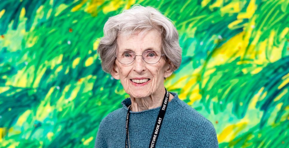 Barbara Elleman stands in front of a green mural by Eric Carle.