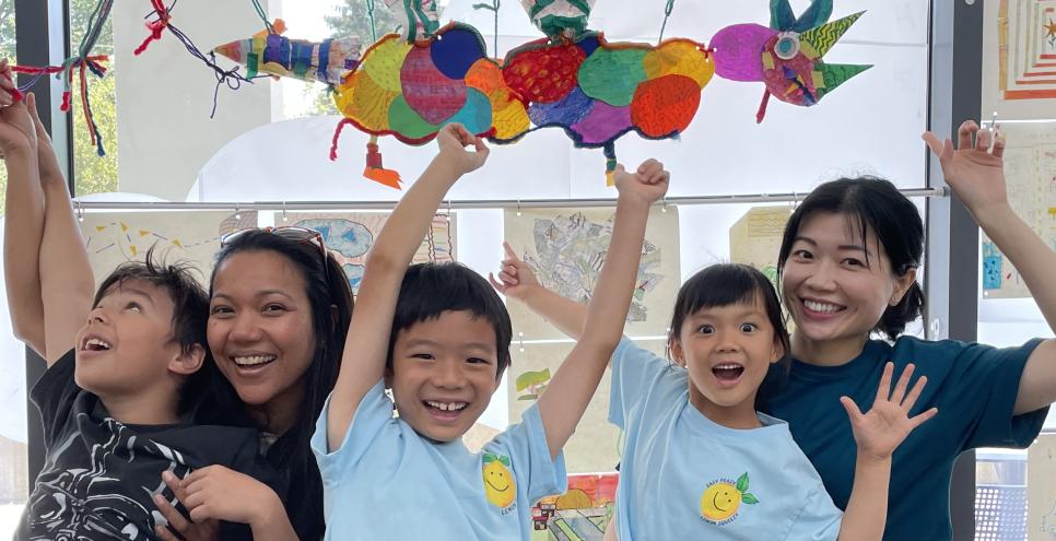 Two adults and three children point above in excitement to their floating paper dragon creation!