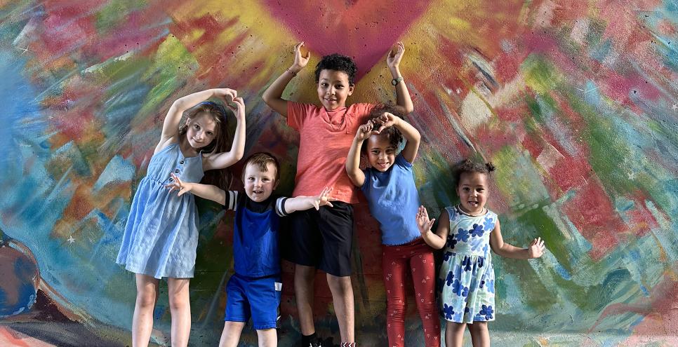 Photograph of children standing in front of heart mural. 