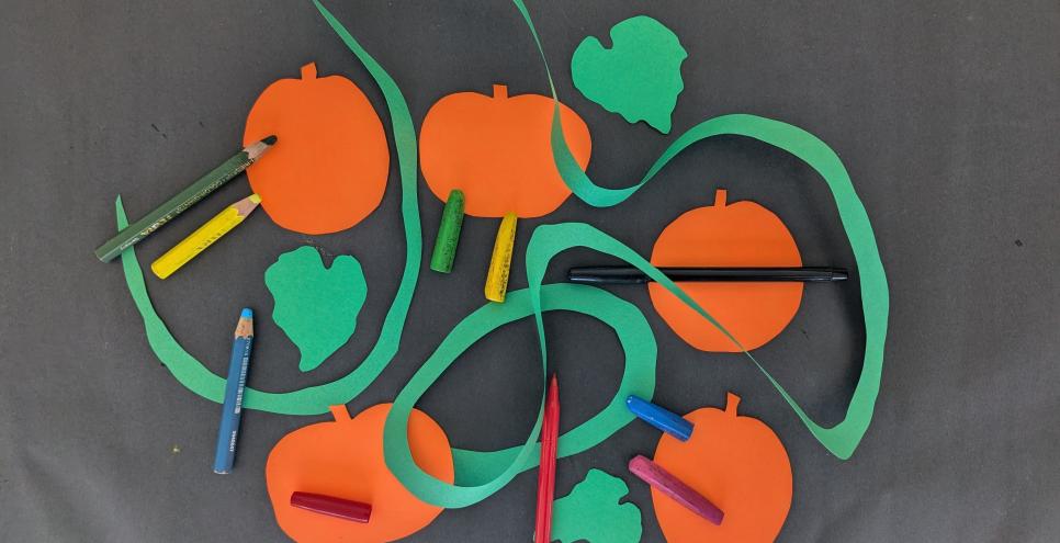 Colorful mark-making tools, orange pumpking paper shapes, green paper pumpkin vines on a table.