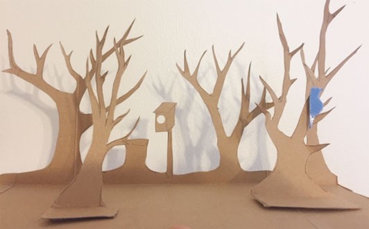 Silhouettes of trees, a birdhouse, and a tree stump cut out of a side of a cardboard box