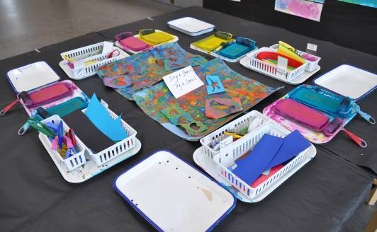 Art studio table with stamp pads, brayers, cutting tools, and scarp papers organized in trays and baskets