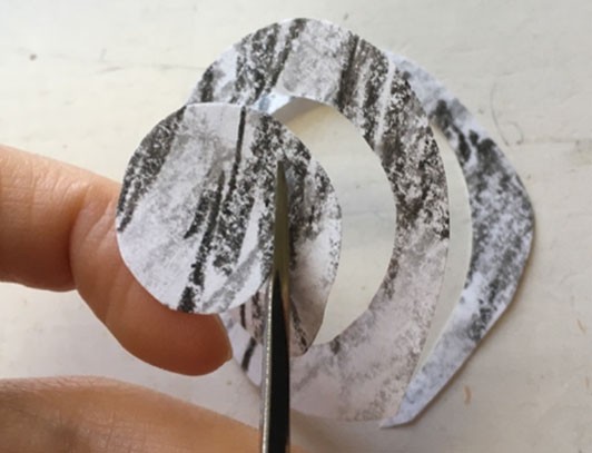 Scissors cutting a spiral out of black, textured paper.