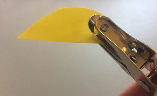 Hole puncher punching into a yellow leaf-shaped paper.