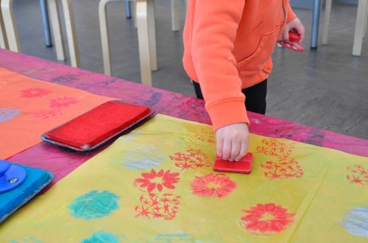 Hand of a child stamping with red onto yellow paper.