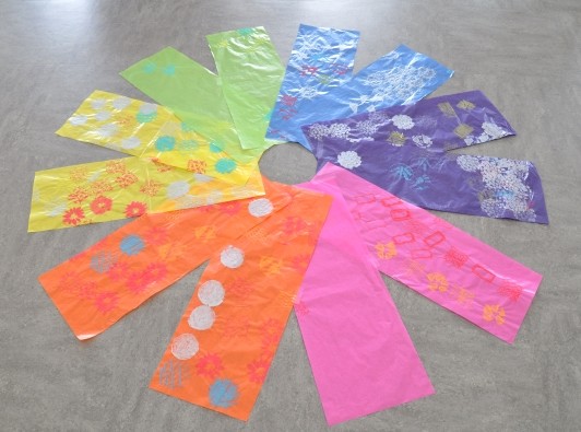 Stamped paper strips organized in rainbow color are laid on the floor in a radial pattern with a hole in the center.